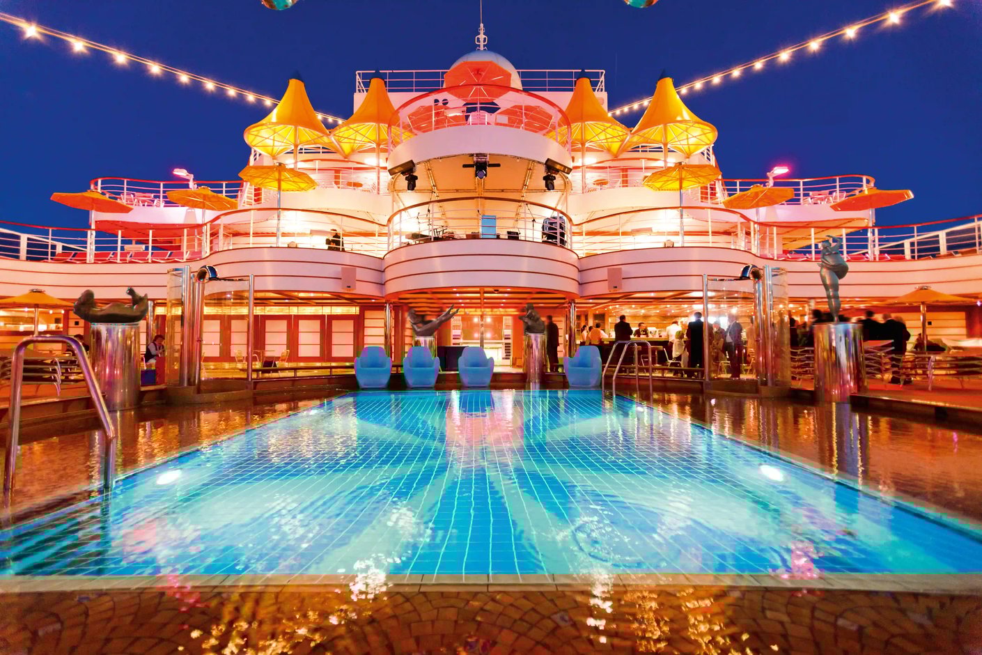 Beleuchteter Poolbereich bei Nacht mit Sitzgelegenheiten und Oberdecks