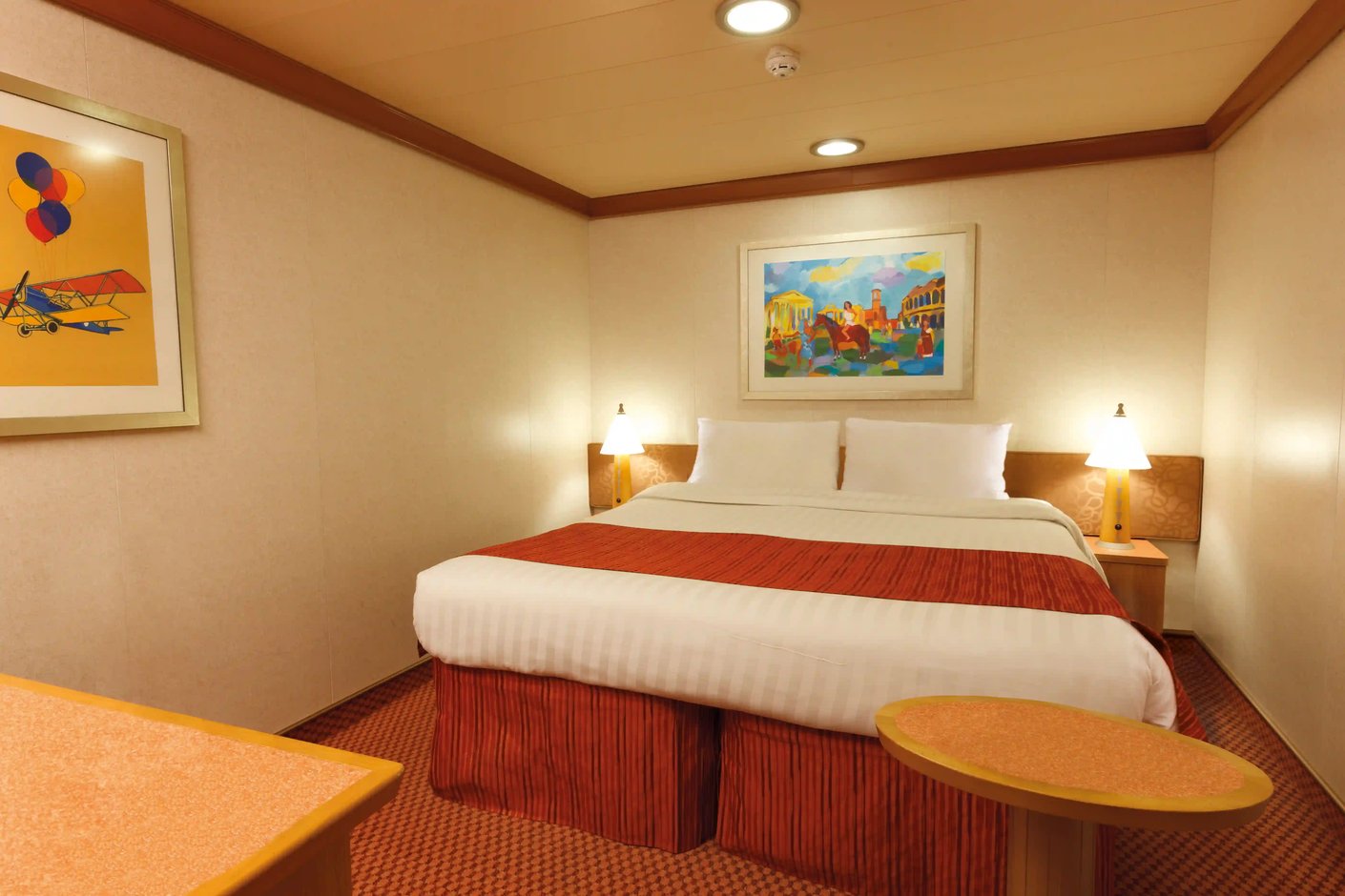 Innenkabine auf Kreuzfahrtschiff mit Doppelbett, Nachttischen und Wandbildern