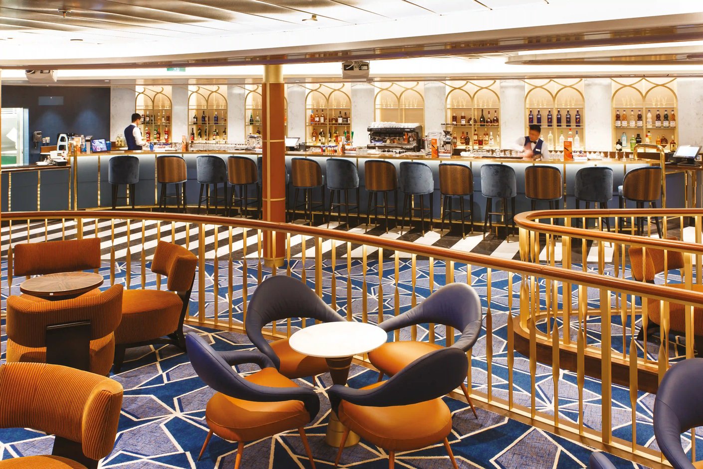 Elegante Schiffsbar mit einer langen Theke, blauen Barhockern und einem Loungebereich mit orange-blauen Sesseln im Vordergrund