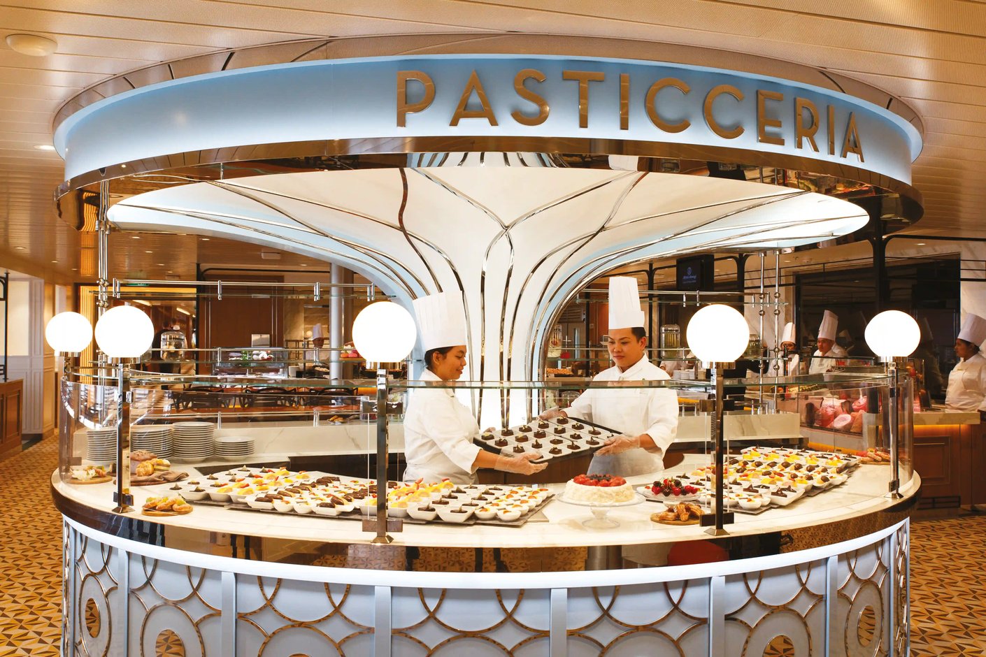 Eine modern gestaltete, runde Pasticceria an Bord mit zwei Angestellten in Kochkleidung hinter einer Verkaufstheke voller Desserts
