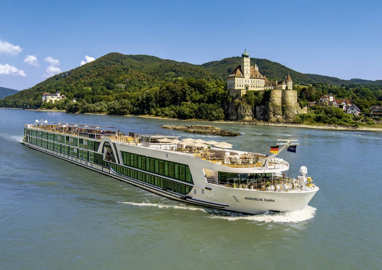 Flusskreuzfahrtschiff auf dem Rhein vor Schloss und Hügeln