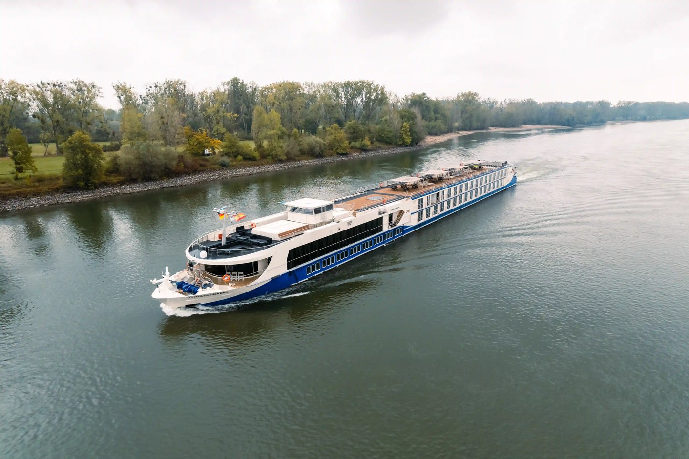 Le MS Charles Dickens navigue sur un fleuve bordé de paysages verdoyants.