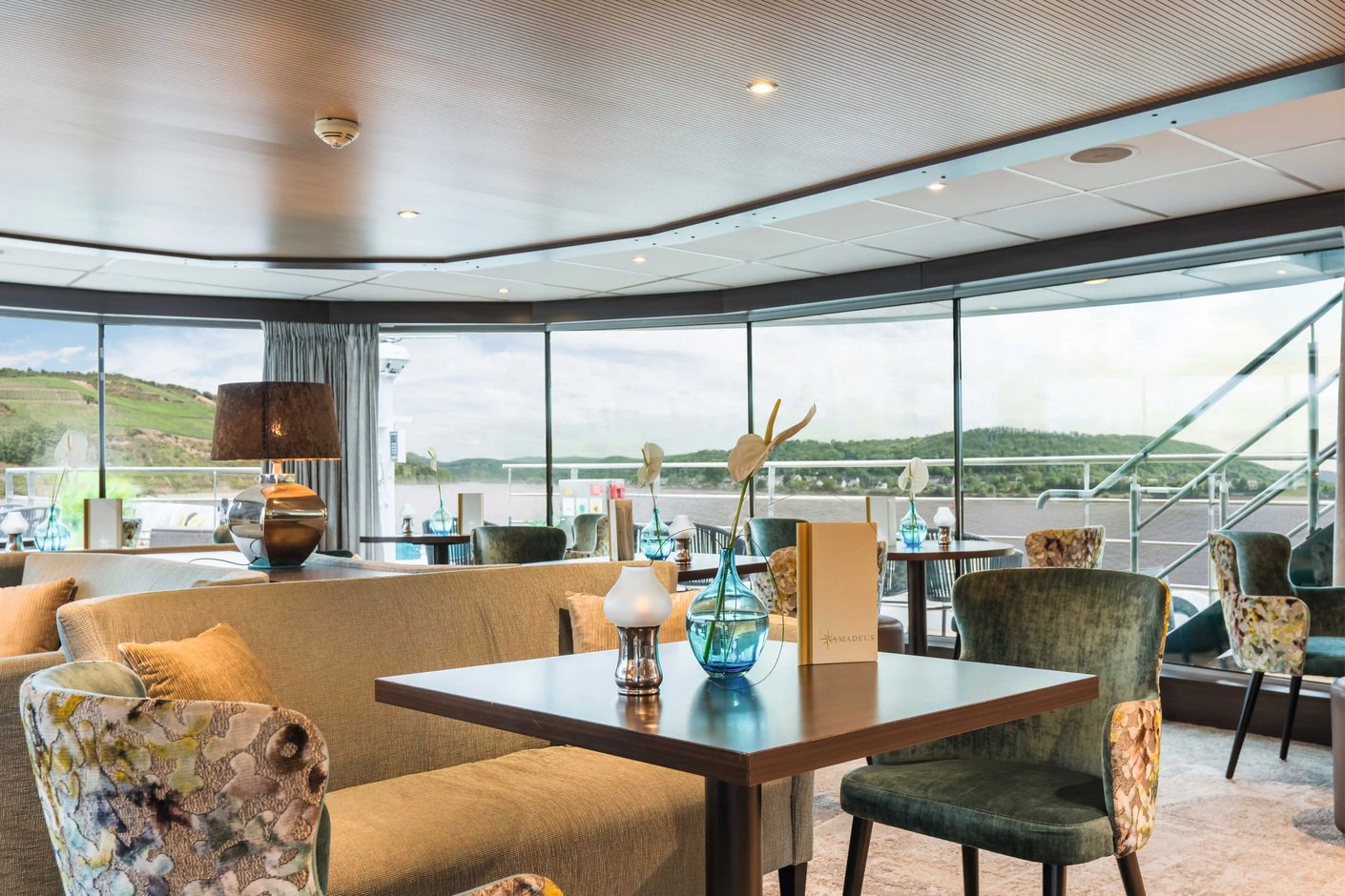 Moderner Barbereich mit Sitzgelegenheiten, gedeckten Tischen, Dekoration und grossen Fenstern mit Flussblick