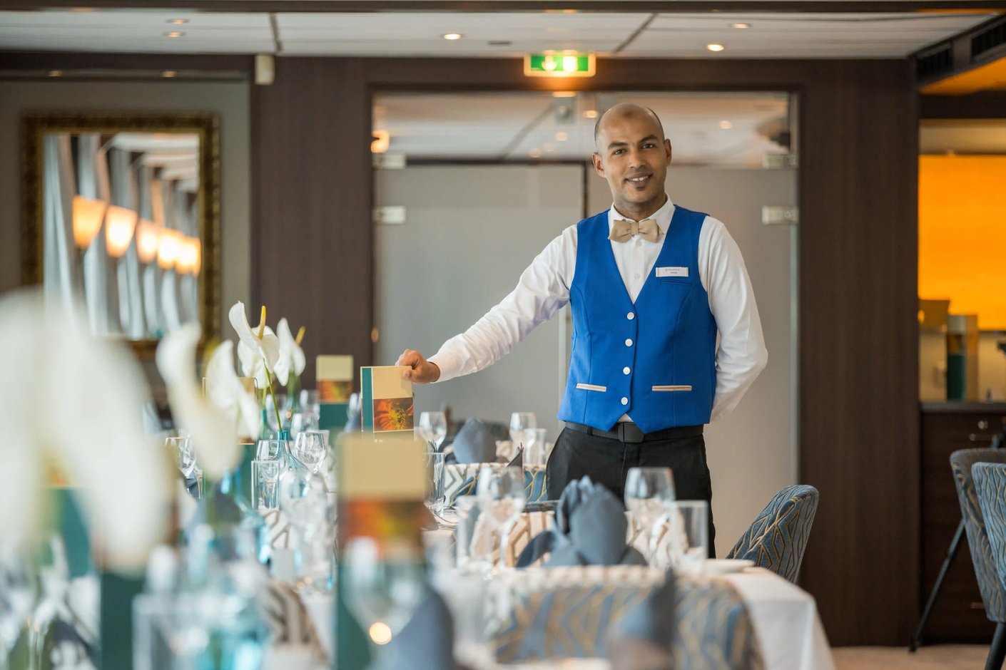 Servicekraft in blauem Veston richtet einen elegant gedeckten Tisch im Bordrestaurant eines Flussschiffes her