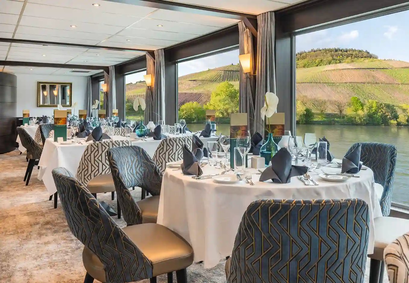 Elegant gedecktes Bordrestaurant mit runden Tischen und Panoramafenstern mit Blick auf Weinberge und Fluss