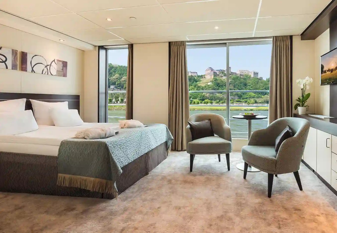 Helle Suite mit Doppelbett, Sitzbereich und bodentiefen Fenstern mit Blick auf Fluss und Landschaft