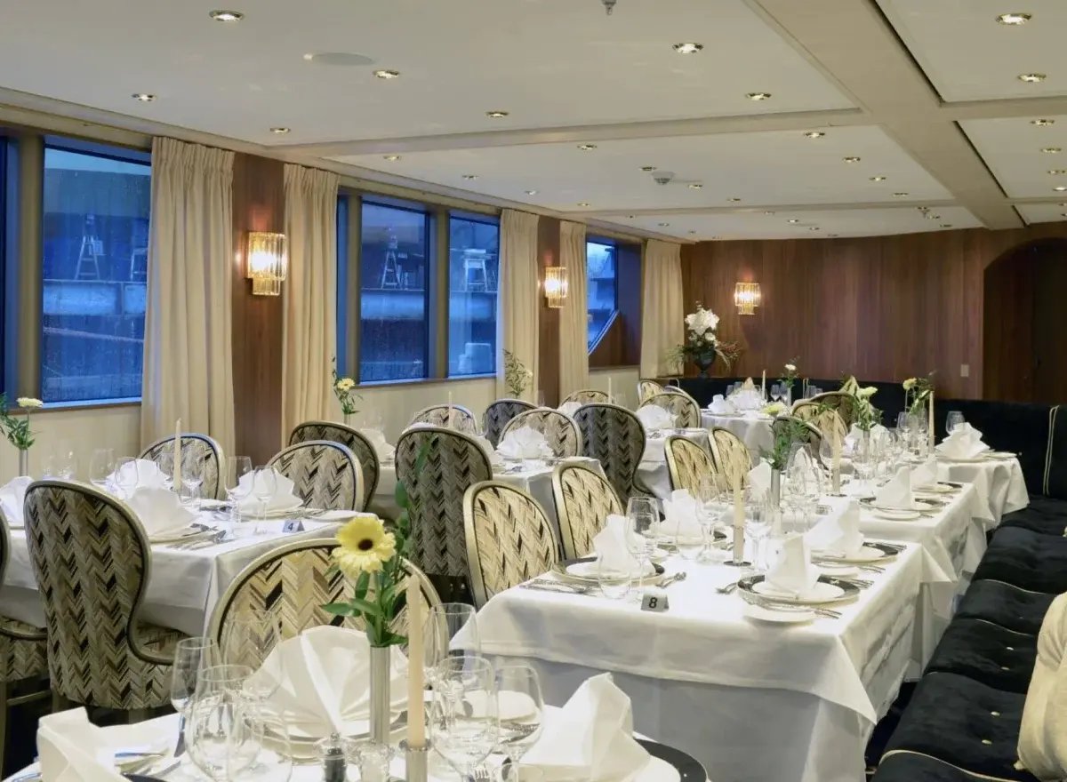 Modernes Schiffsrestaurant mit fein gedeckten Tischen, dunklen Stühlen und grossen Panoramafenstern.