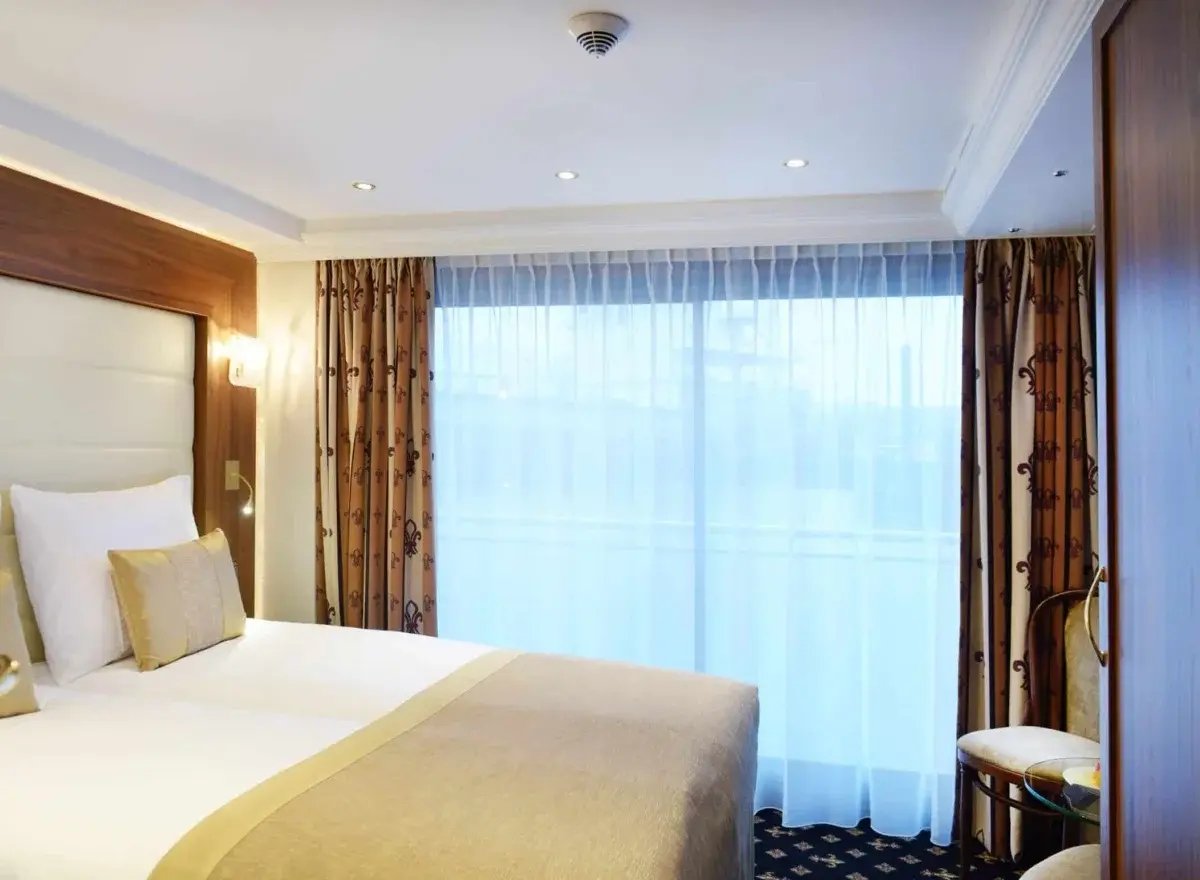 Luxuriöse Kabine mit Doppelbett, Sitzecke und einem französischen Balkon mit Blick auf die Landschaft.