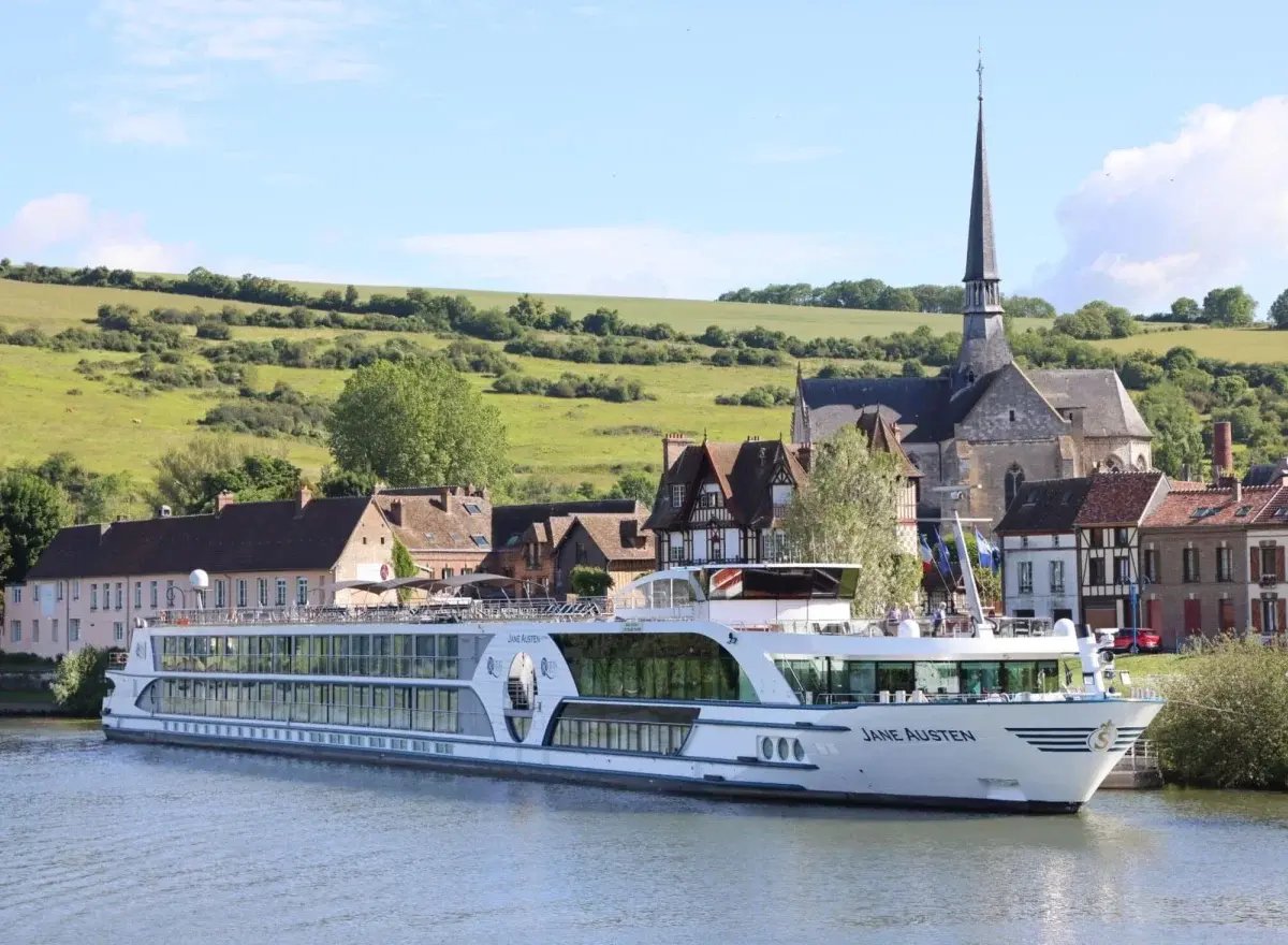 Das Flusskreuzfahrtschiff MS Jane Austen fährt auf einem breiten Fluss vor einer bewaldeten Hügellandschaft.