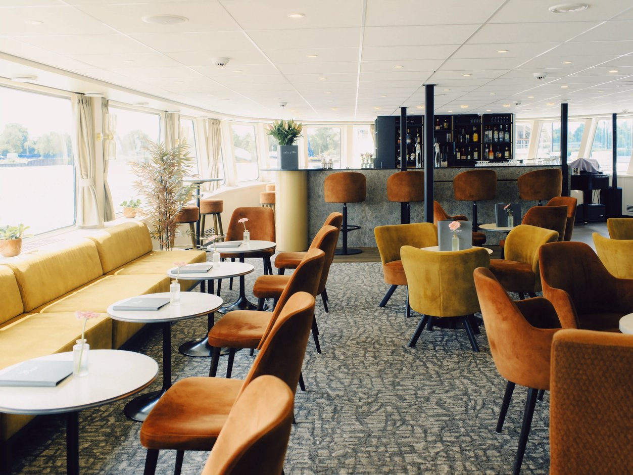 Panorama-Lounge mit Sesseln, Sofas und Bar sowie grossen Fenstern mit Flussblick.