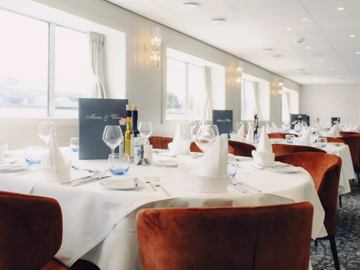 Elegant gedeckter Restaurantbereich mit runden Tischen und roten Sesseln an Bord