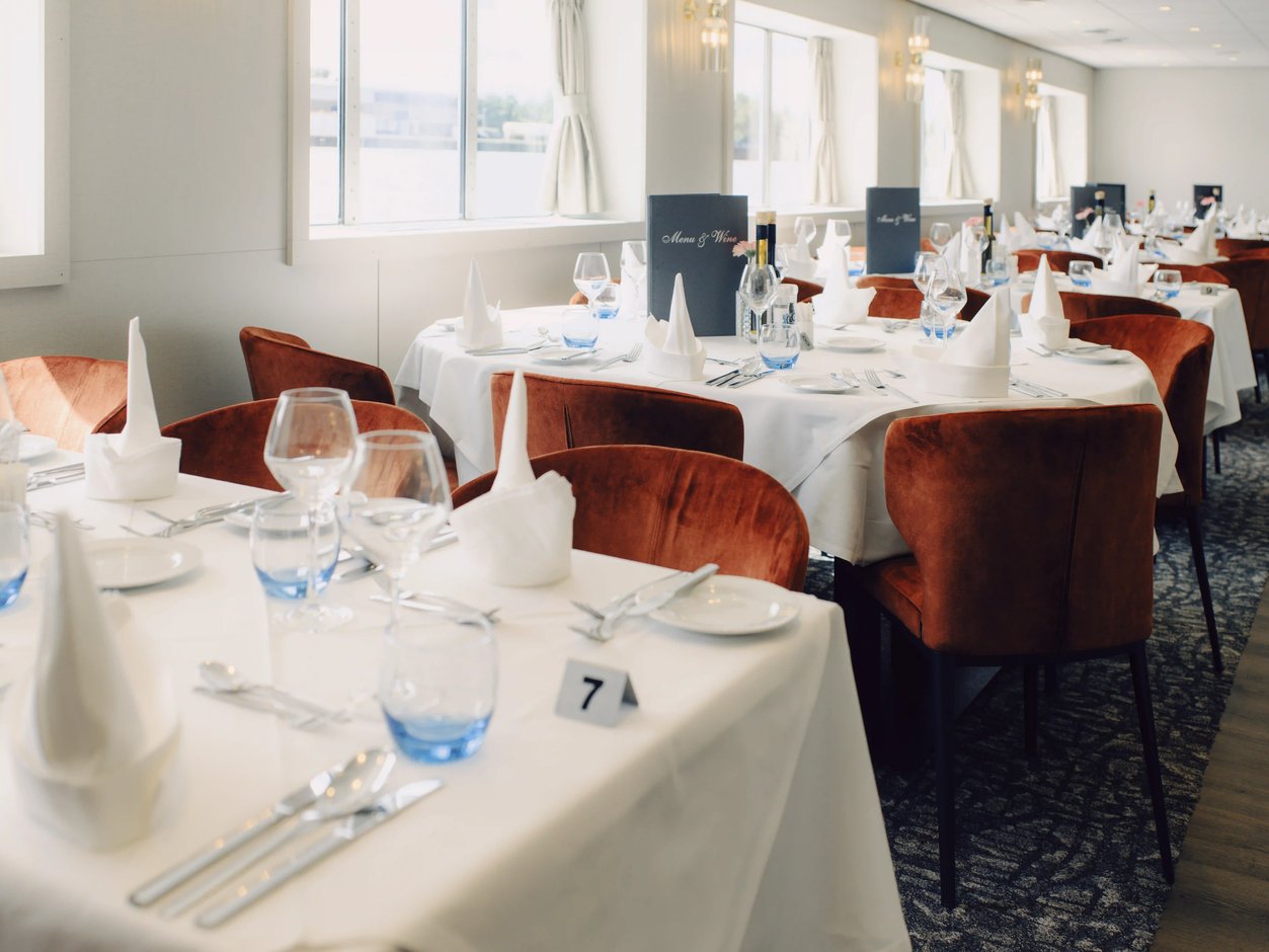 Restaurant des Schiffes mit weiss eingedeckten Tischen und roten Sesseln entlang der Fensterfront