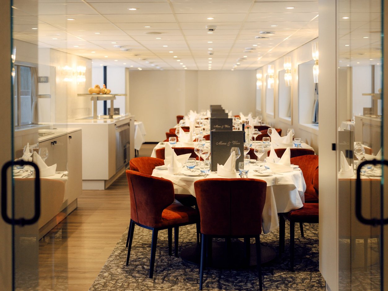 Elegant gedeckter Restaurantbereich mit runden Tischen und roten Sesseln an Bord