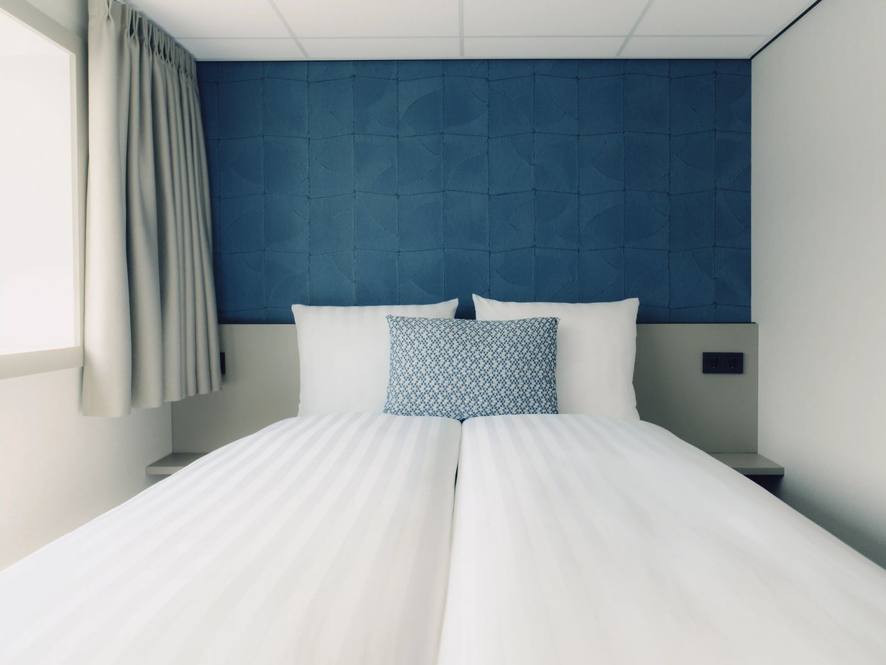 Doppelbett in einer Kabine mit blau gepolsterter Rückwand und Fenster.