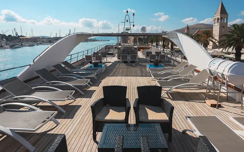 Sonnendeck eines Kreuzfahrtschiffes mit Sitzgruppe und Blick auf den Hafen