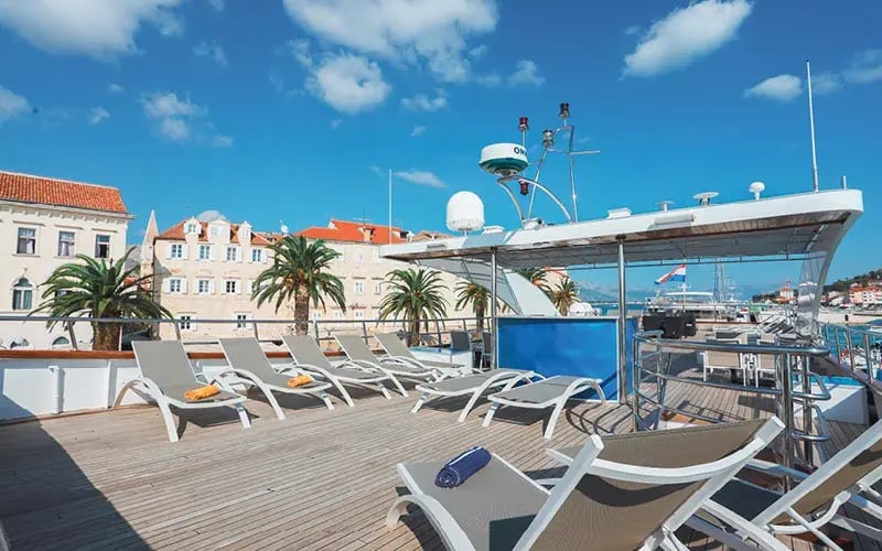 Sonnendeck eines Kreuzfahrtschiffes mit Liegen und Blick auf Küstenstadt