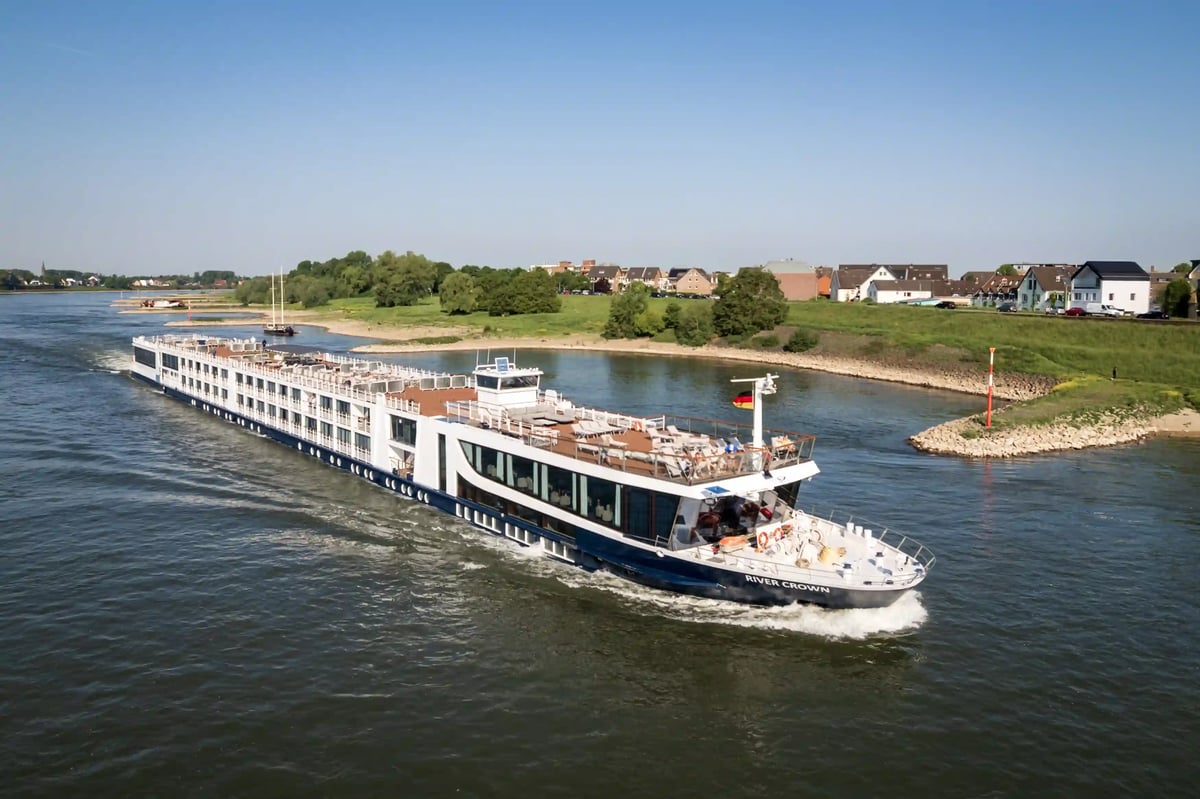 Elegantes Flusskreuzfahrtschiff fährt auf einem breiten Fluss durch eine grüne Uferlandschaft