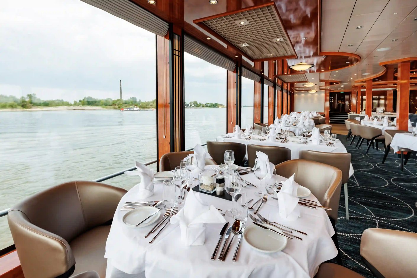 Stilvolles Bordrestaurant mit gedeckten Tischen und großen Panoramafenstern entlang des Flusses