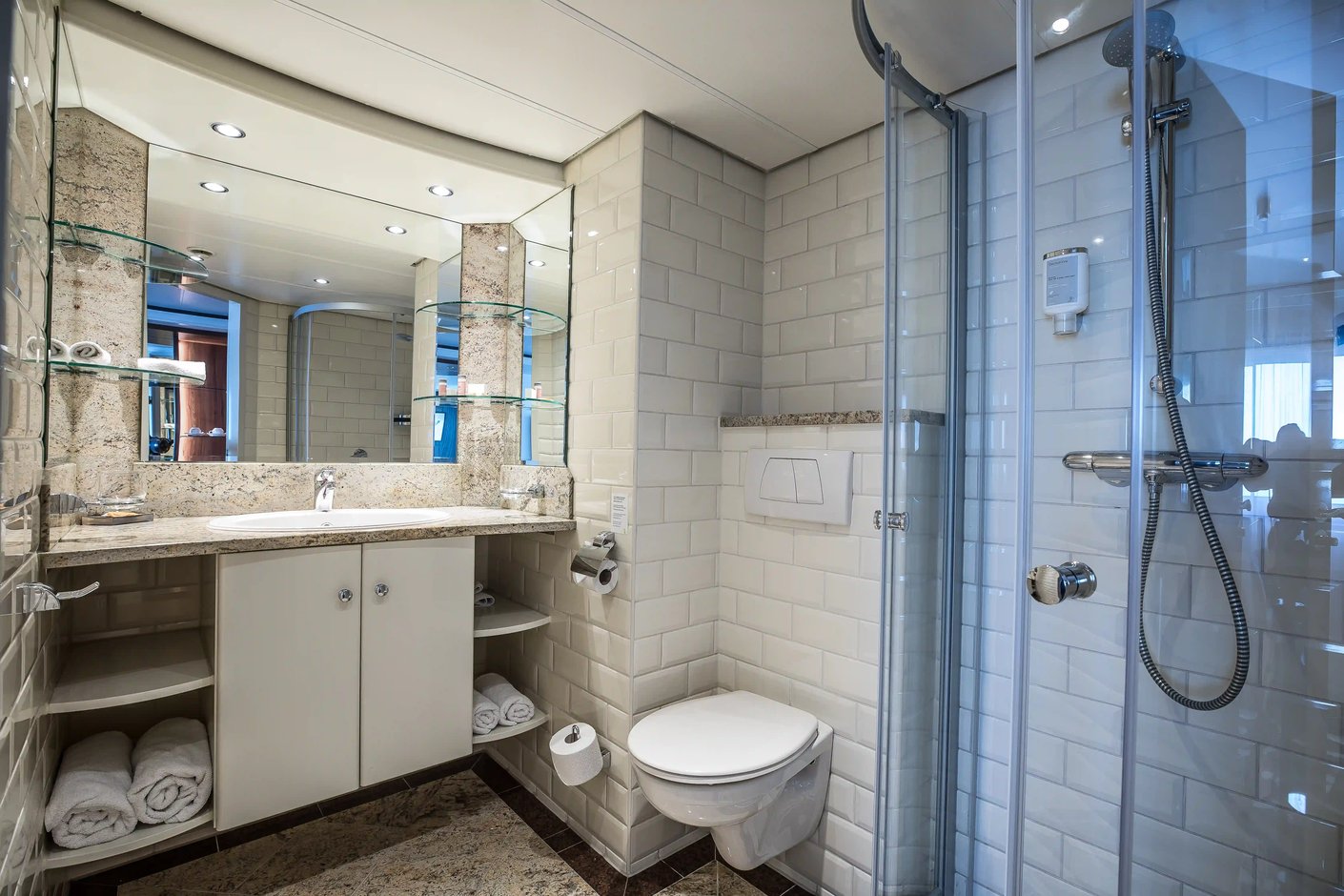 Funktionales Badezimmer einer Schiffskabine mit Dusche, Waschbecken, Spiegel und WC