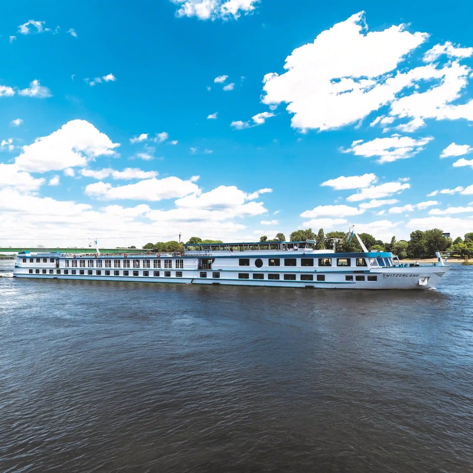 Das weisse Flussschiff MS Switzerland fährt bei blauem Himmel und Sonnenschein auf einem breiten Fluss.
