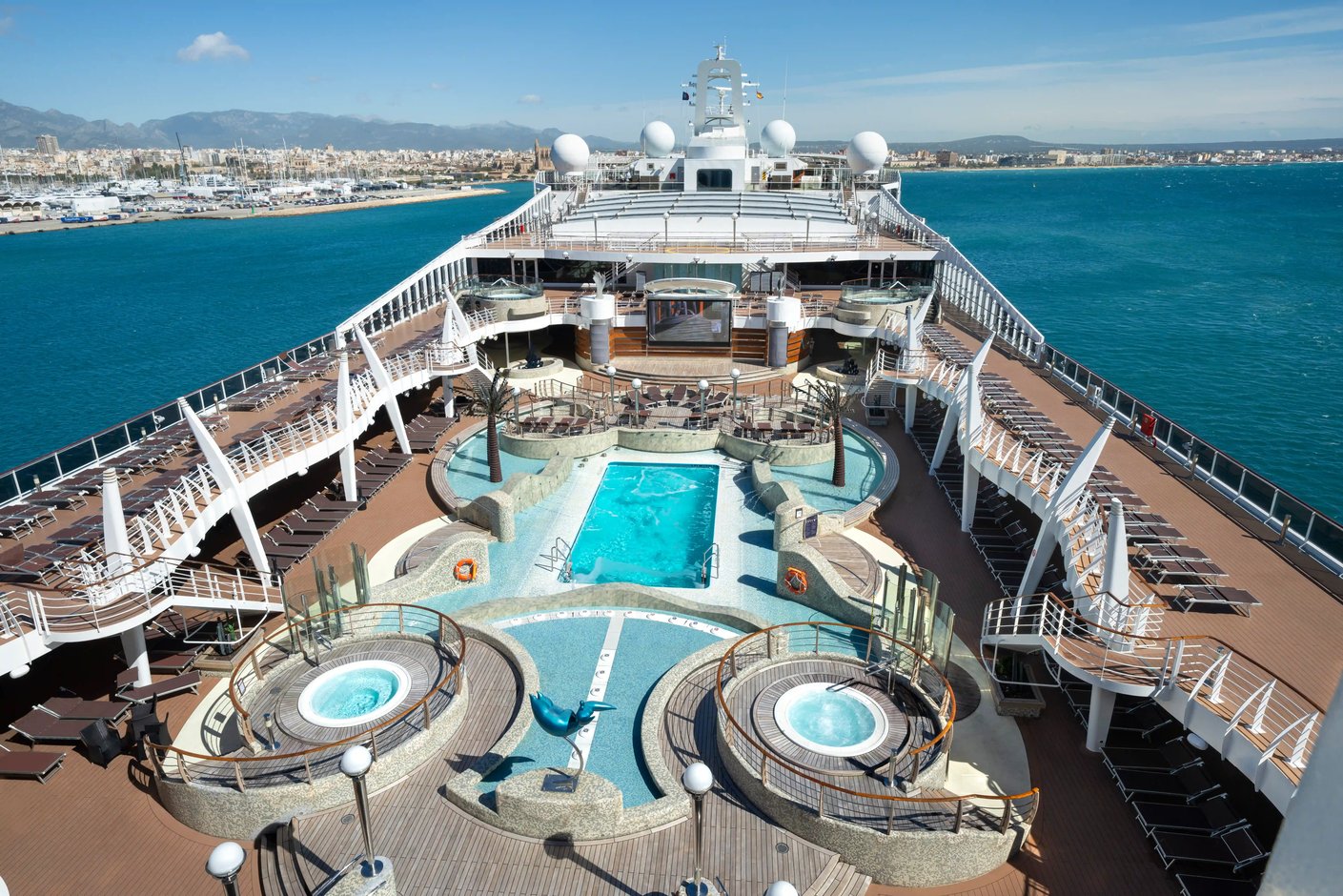 Pooldeck der MSC Fantasia mit zentralem Pool, Whirlpools, Sonnenliegen und Blick auf den Hafen und das Meer.
