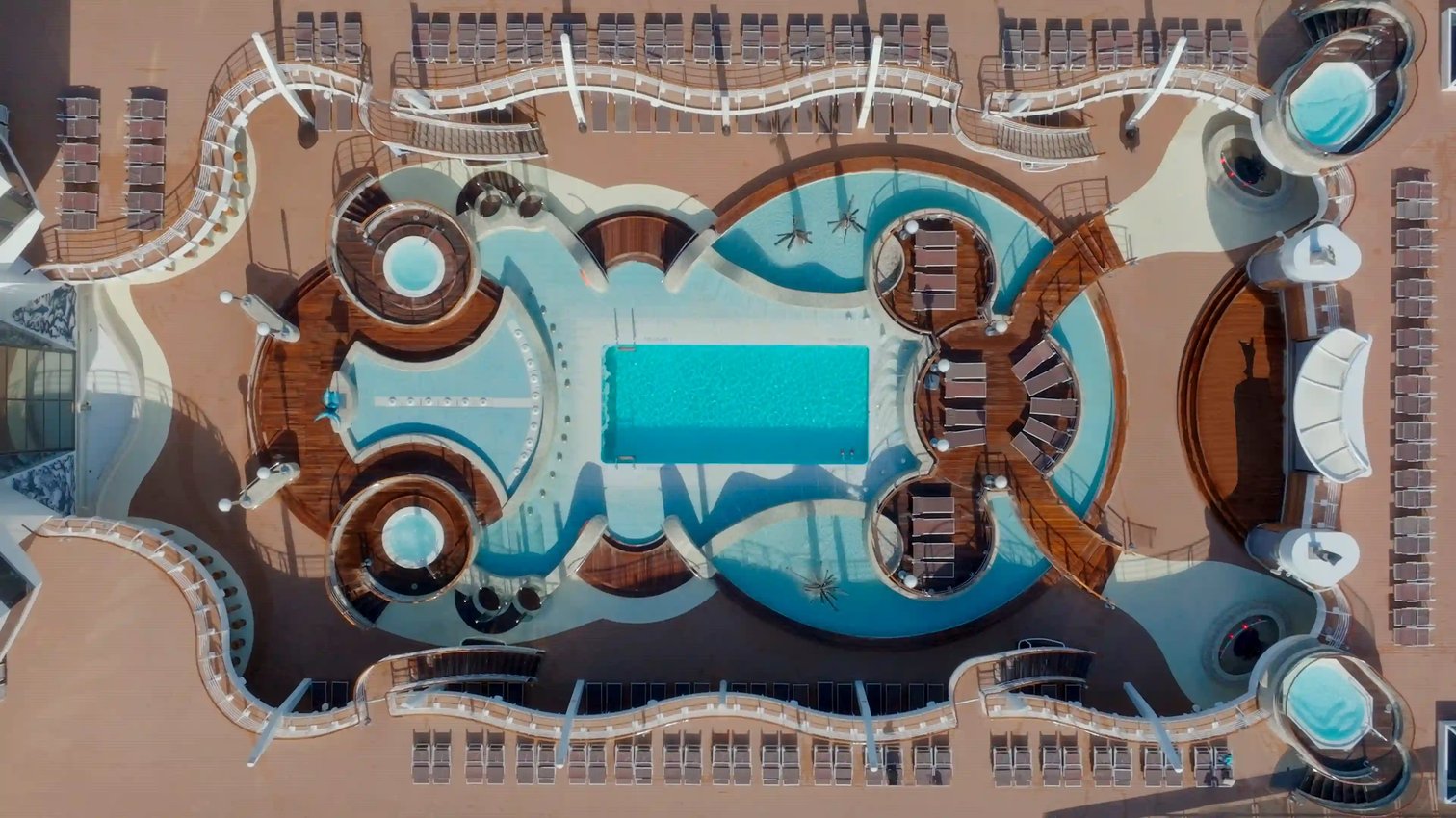 Luftaufnahme der grosszügigen Poolarea auf der MSC Fantasia mit zentralem Pool, Whirlpools, Sonnenliegen und geschwungenem Deckdesign.