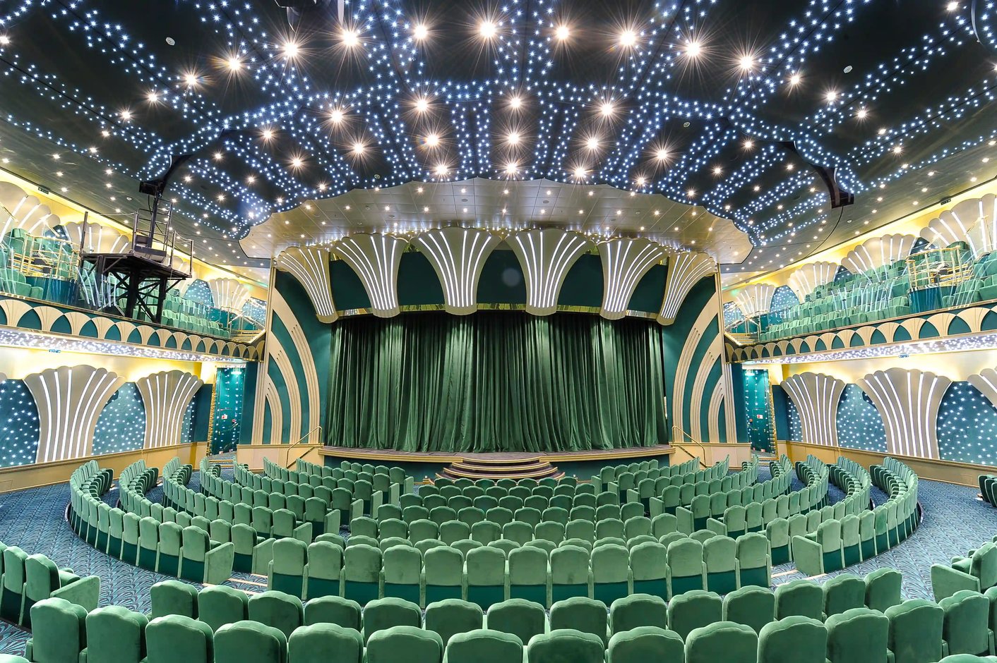 Grosses Theater der MSC Magnifica mit gruenen Sitzreihen, beleuchteter Decke und geschlossener Bühne.