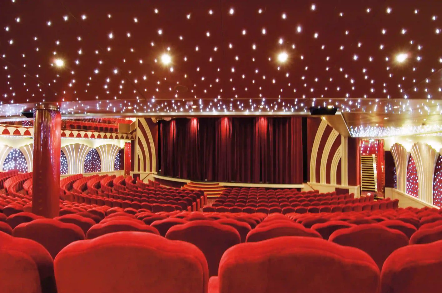 Theater der MSC Musica mit dekorativer Decke, warmem Licht, rotem Vorhang und geschwungener Buehne