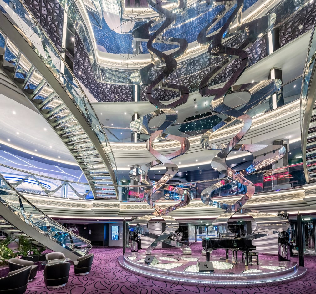 Modernes Atrium auf der MSC Virtuosa mit geschwungenen Treppen, spiegelnden Designelementen und mehreren offenen Decks