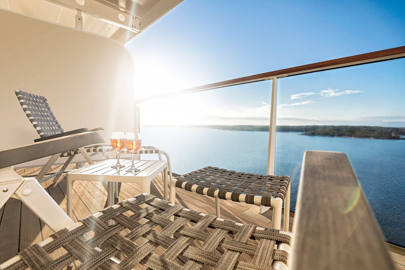 Balkon mit Liegen, kleinem Tisch und Gläser, Blick auf das Meer bei Sonnenschein