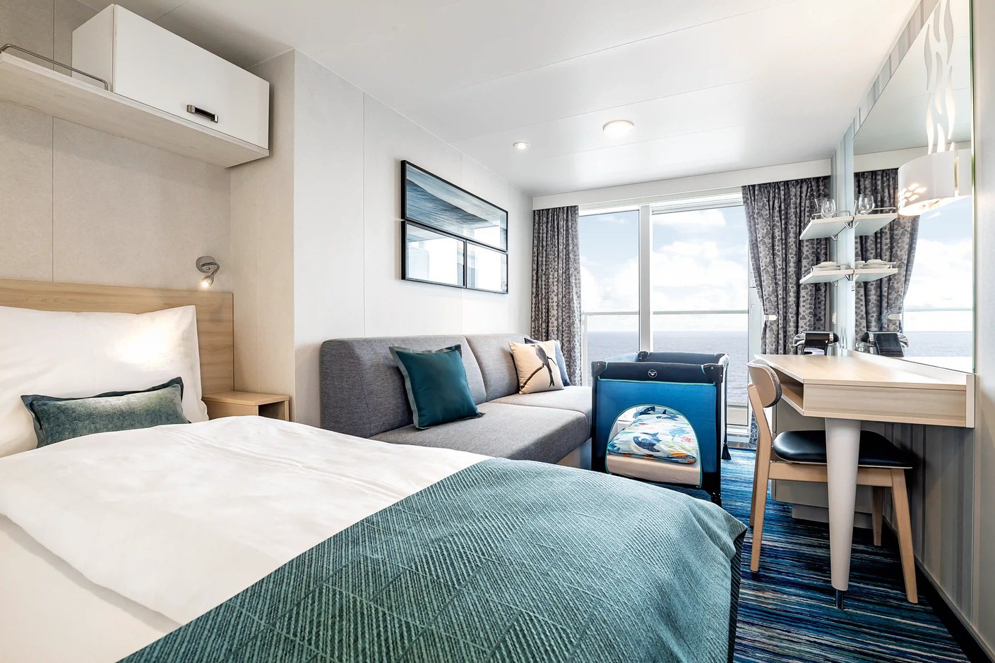 Balkonkabine mit Doppelbett, Sofa, Schreibtisch und Zugang zum Balkon mit Meerblick