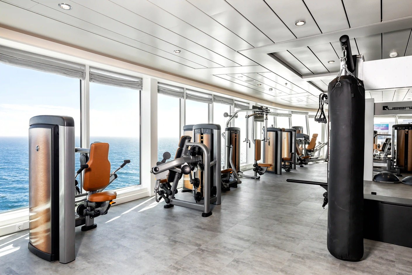 Fitnessraum mit Trainingsgeräten, Boxsack und Panoramafenstern mit Meerblick