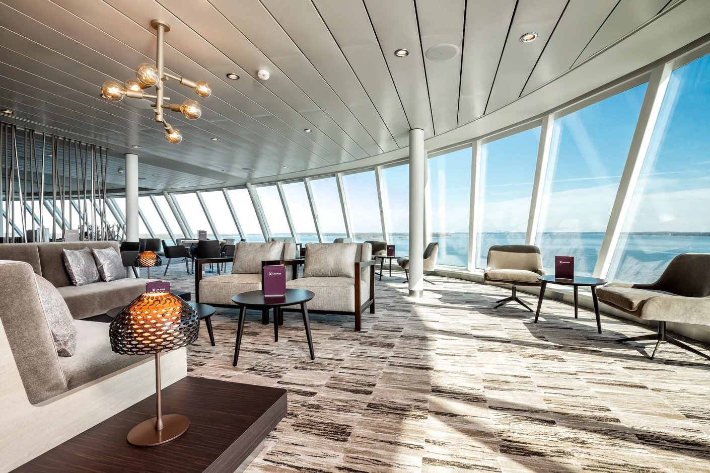 Exklusive Lounge mit Sesseln, Tischen und Panoramafenstern mit Meerblick