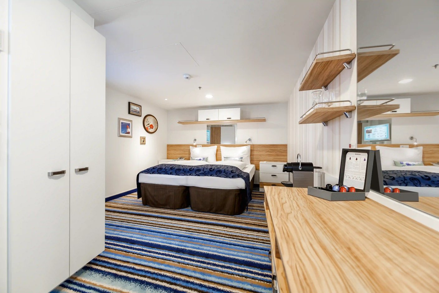 Innenansicht einer Innenkabine auf der Mein Schiff 3 mit einem Doppelbett, einem Kleiderschrank, einem Schreibtisch und einer Nespresso-Maschine.
