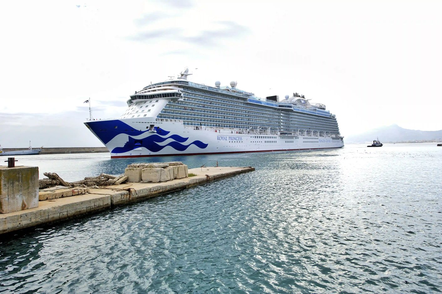 Das Kreuzfahrtschiff Royal Princess liegt an einer Hafenmole im ruhig fließenden Wasser unter leicht bewölktem Himmel.