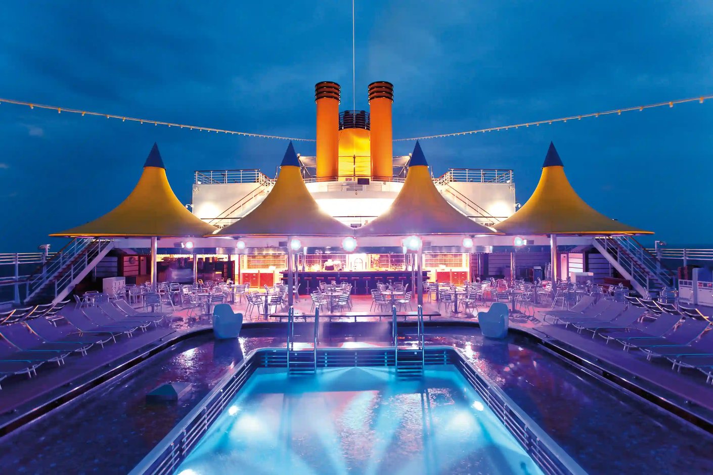 Pooldeck der Costa Deliziosa bei Nacht mit beleuchtetem Pool, Bar und Sitzplätzen