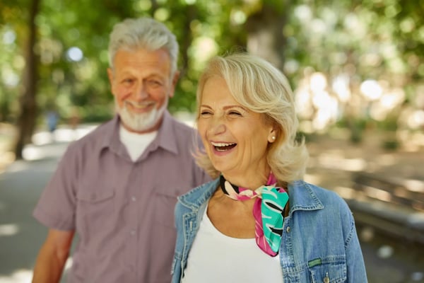 Lachendes älteres Paar spaziert gemeinsam durch eine grüne Parklandschaft