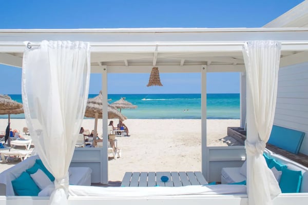 Strandlounge mit weißen Vorhängen und Blick auf das Meer an einem Sandstrand.