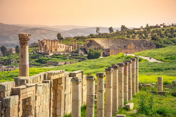 Antike Ruinen von Jerash mit Säulenstraße und Amphitheater in grüner Landschaft.