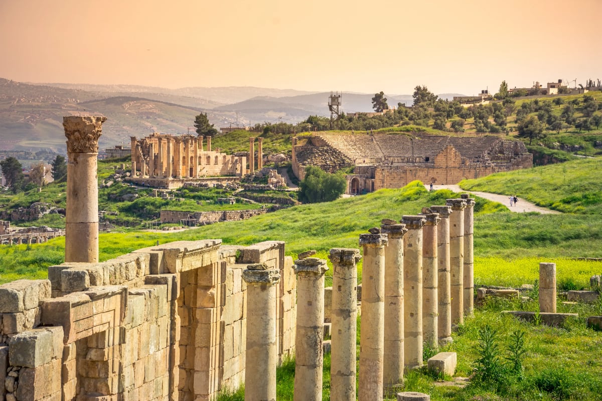 Ruines antiques de Jerash avec colonnades et amphithéâtre dans un paysage verdoyant.