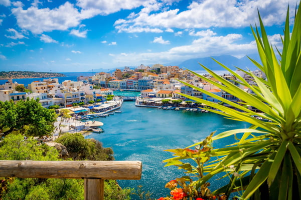 Blick auf den Hafen von Agios Nikolaos mit Booten, Promenade und türkisfarbenem Meer vor hügeliger Landschaft