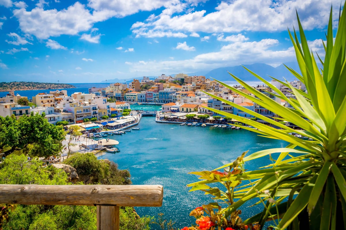 Blick auf den Hafen von Agios Nikolaos mit Booten, Promenade und türkisfarbenem Meer vor hügeliger Landschaft