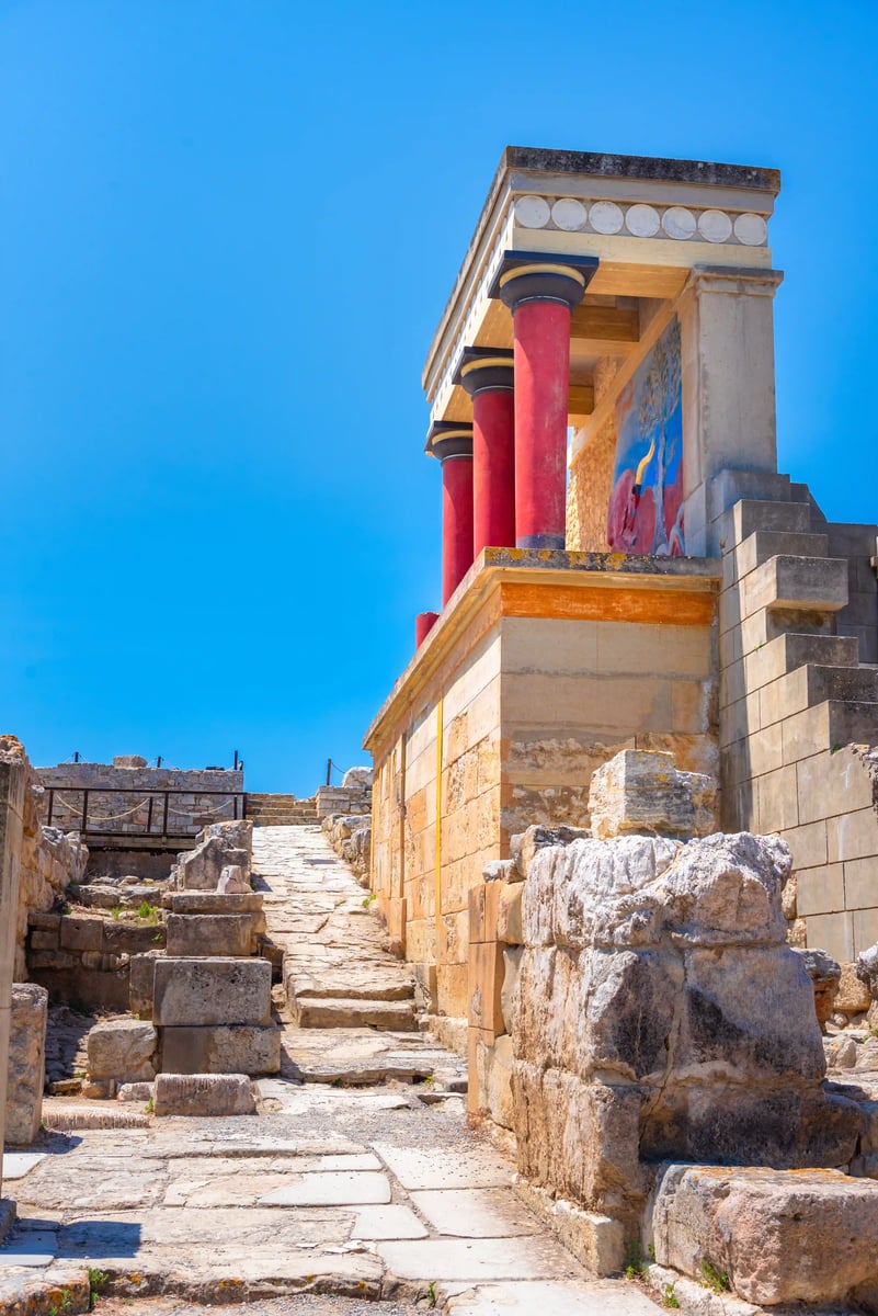 Reste des Palastes von Knossos mit roten Säulen und steinernem Weg unter blauem Himmel