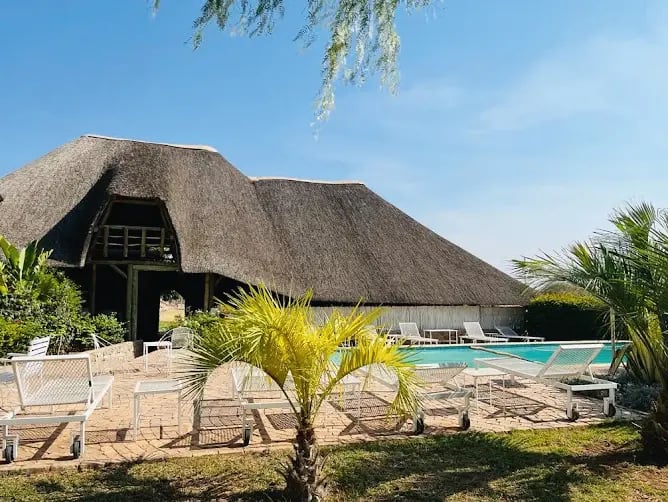 Lodge mit traditionellem Reetdach, Pool und Terrasse inmitten tropischer Vegetation.
