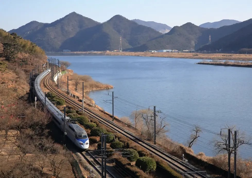 KTX-Hochgeschwindigkeitszug fährt entlang eines Flusses durch die Berglandschaft Südkoreas.