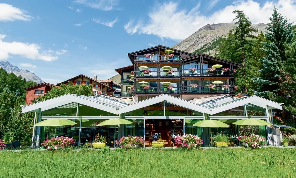 Hotel Pirmin Zurbriggen im Wallis mit blumengeschmückten Balkonen, Sonnenterrasse und Bergkulisse.