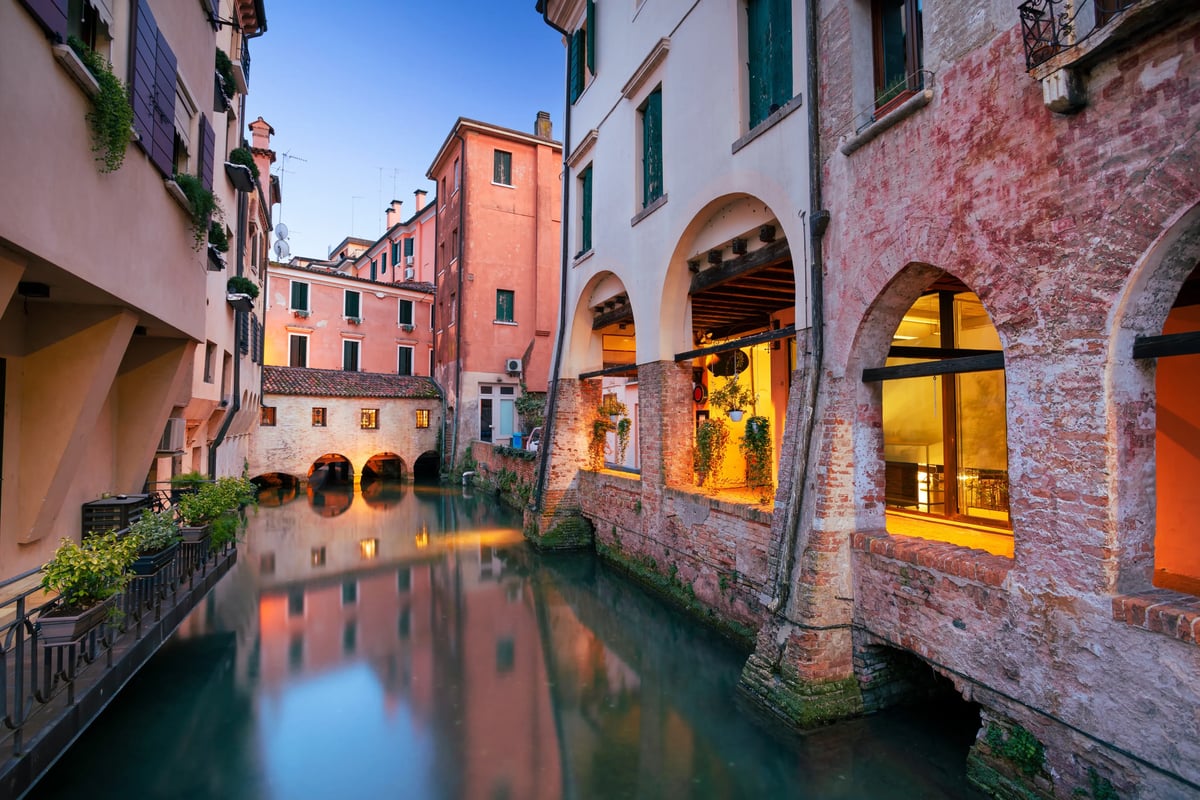 Malerischer Kanal in der Altstadt von Treviso mit historischen Häusern und beleuchteten Arkaden.