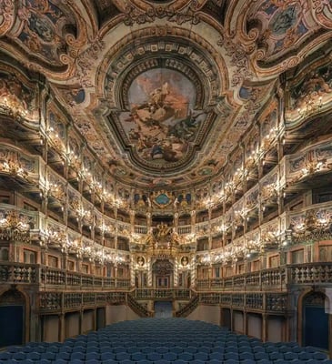 Prunkvoller Theatersaal mit reich verziertem Deckengemälde, goldenen Logen und Reihen blauer Sitze.