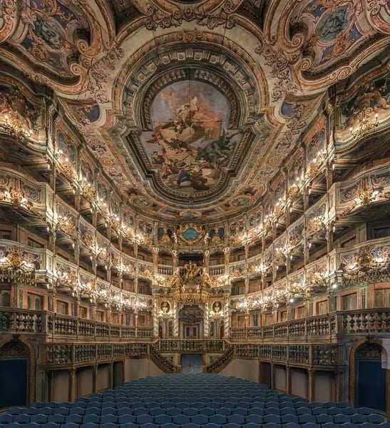 Prunkvoller Theatersaal mit reich verziertem Deckengemälde, goldenen Logen und Reihen blauer Sitze.