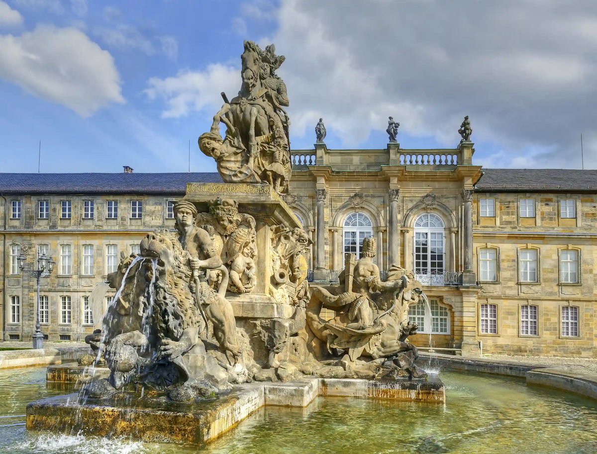 Barocker Brunnen mit Figuren und fliessendem Wasser vor der Fassade des Neuen Schlosses.